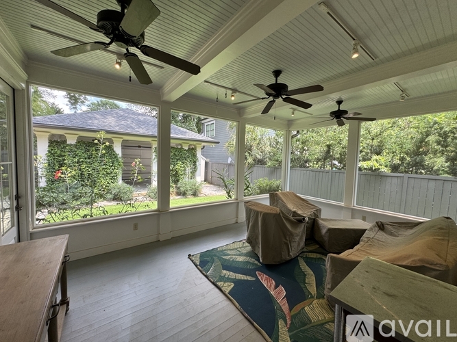 A sunroom with a ceiling fan and a view of a house and trees.