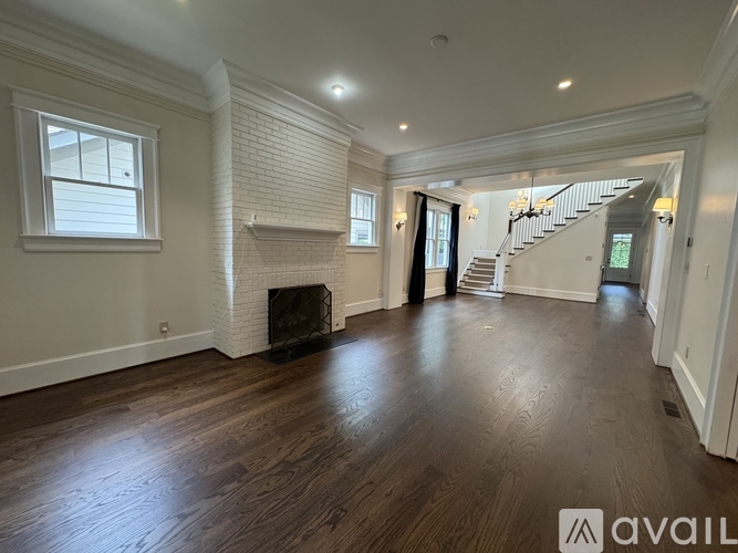 A spacious room with wooden floors and a staircase in the background.