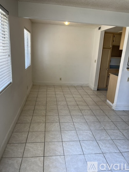 A room with white walls and tile flooring, with a doorway leading to another room.