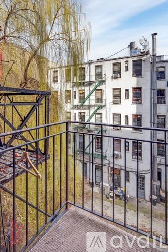 A balcony with a black railing and a tree in the background.