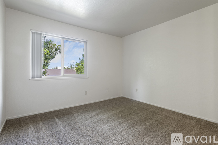 A room with a carpeted floor and a window showing a view of a house and trees outside.