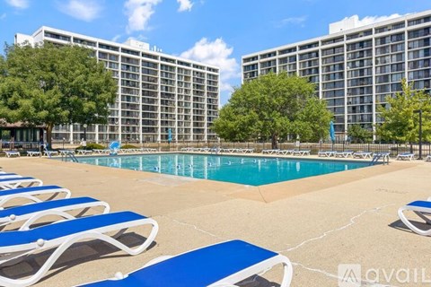 A pool area with sun loungers and a large building in the background.