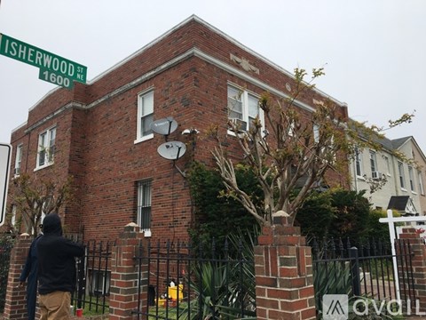 A man in a black hoodie is walking past a red brick building with a satellite dish on the roof.