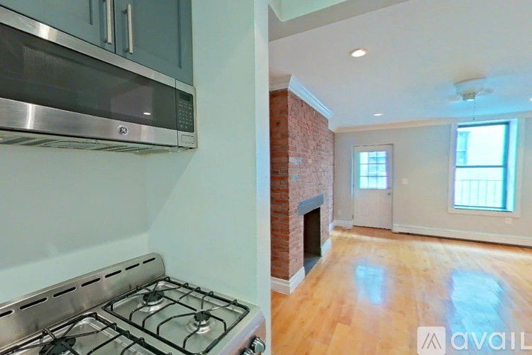A kitchen with a stove top oven and a brick fireplace in the living room.