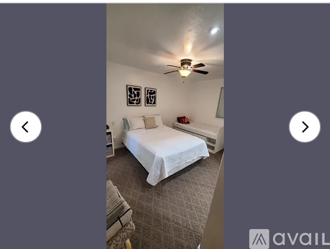 A bedroom with a bed, pillows, a ceiling fan, and pictures on the wall.