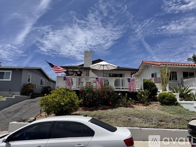 A white car is parked in front of a house with an American flag hanging on the front porch.