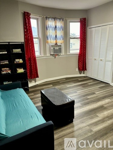 A room with a bed, ottoman, and bookshelf.
