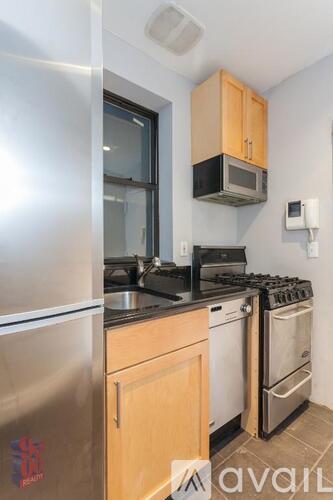 A kitchen with a stainless steel refrigerator, a microwave above the stove, and wooden cabinets.
