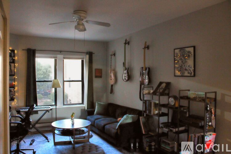 A living room with a couch, a coffee table, a guitar, a fan, and a window.