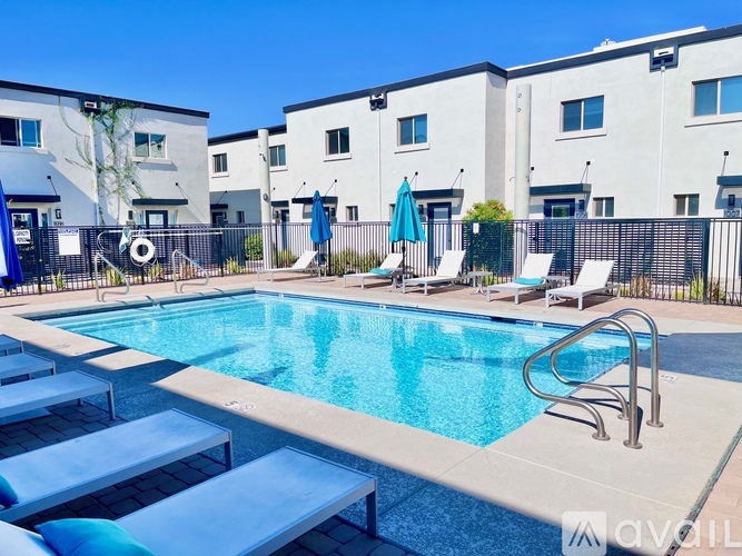 A pool with sun loungers and a fence in front of apartment buildings.