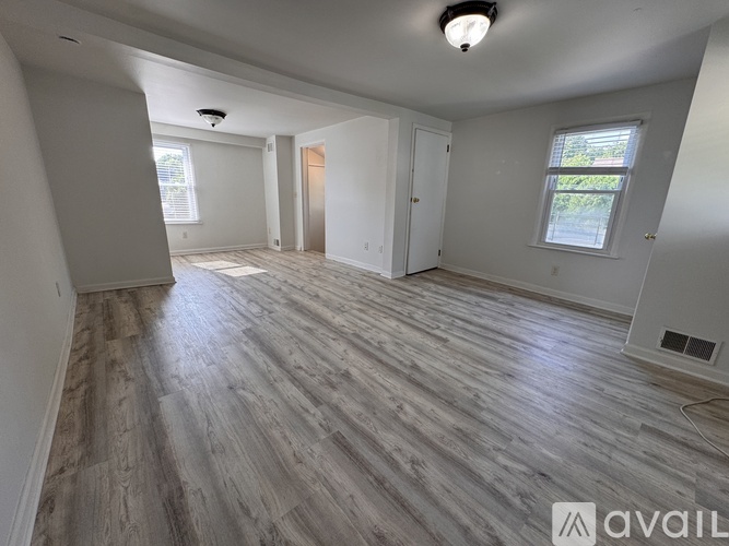 A spacious room with wooden flooring and white walls.