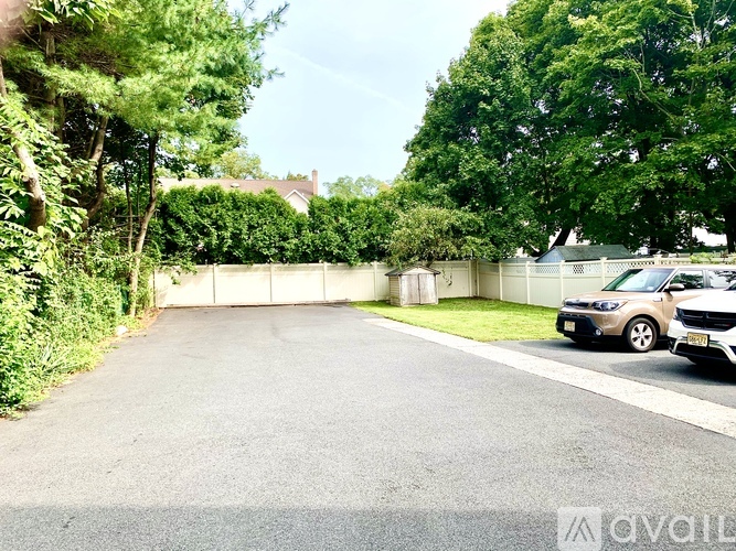 A car is parked on the side of a road with a white fence and greenery on the side.