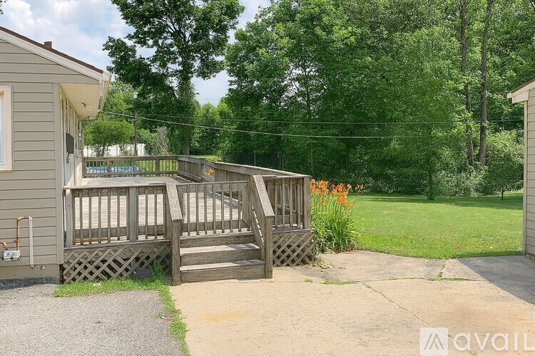 A wooden deck leads to a house with a gravel driveway and a green lawn.