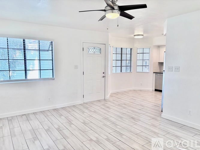 A spacious room with a ceiling fan and light, hardwood flooring, and a door leading to another room.
