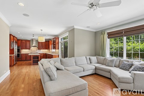A spacious living room with a grey sectional sofa and a kitchen area in the background.