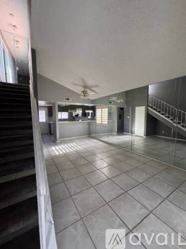 A spacious room with a staircase on the left and a ceiling fan in the middle.