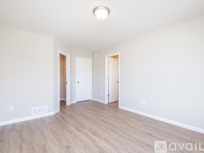 A spacious room with wooden floors and white walls, featuring two doors and a single light fixture on the ceiling.