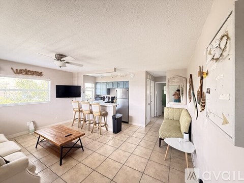 A living room with a wooden table and chairs, a flat screen TV, and a kitchen area in the background.