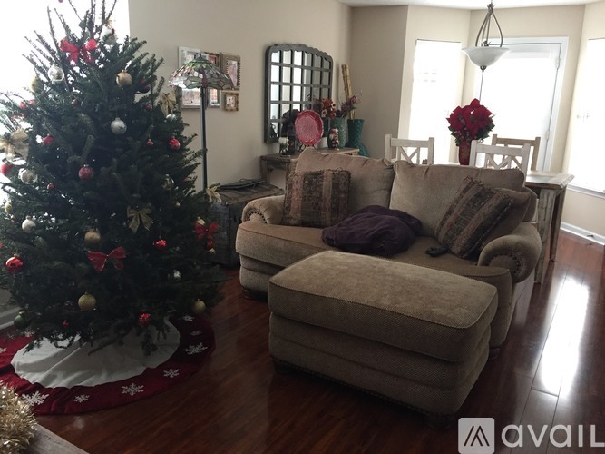 A Christmas tree with red and gold ornaments sits in a living room with a couch and a chair.