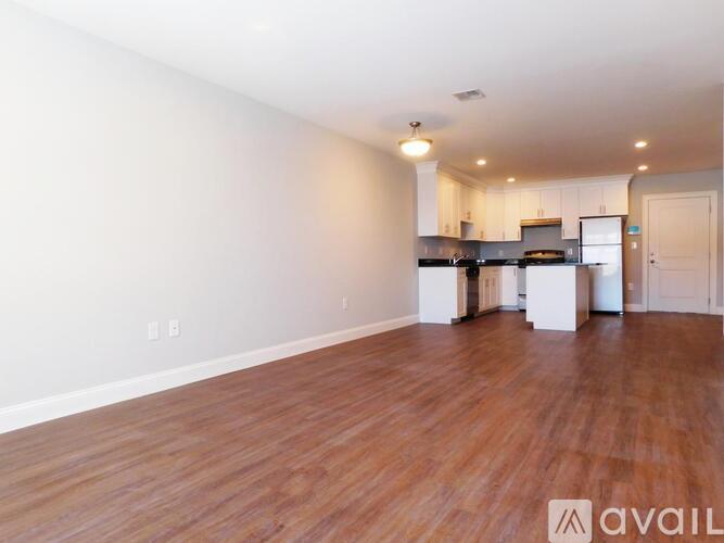 A spacious living room with wooden flooring and a kitchen area in the background.