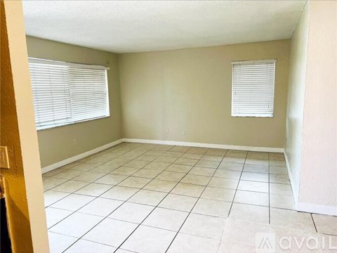 A room with tiled flooring and two windows with blinds.