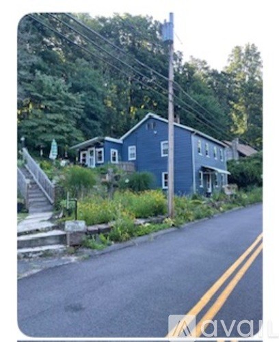 A blue house with a white door and windows is surrounded by greenery.