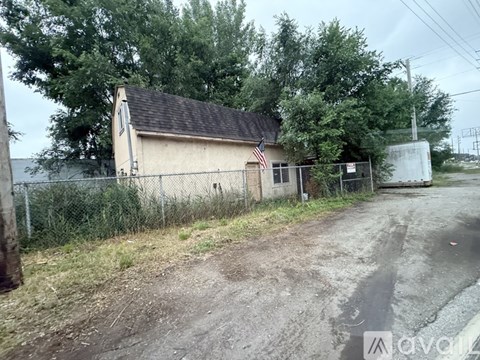 A small building with an American flag on it is surrounded by a fence and trees.