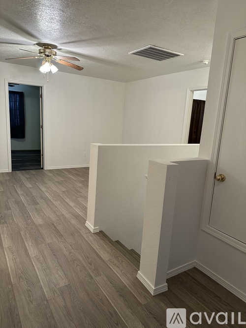 A room with a ceiling fan and light fixture, and a door with a gold handle.