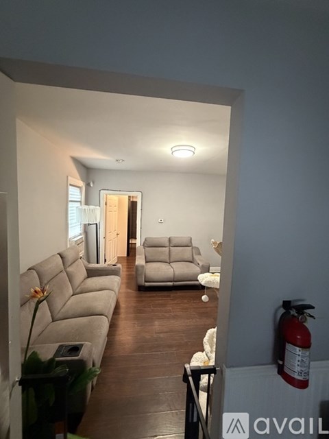 A living room with a grey couch and a fire extinguisher on the wall.