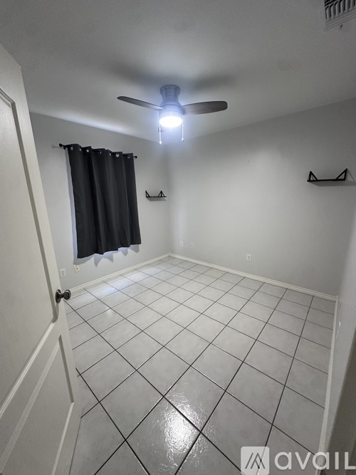 A room with a ceiling fan and a window with black curtains.