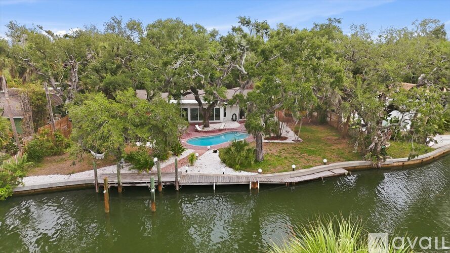 A house with a pool is surrounded by trees and is on a dock over water.