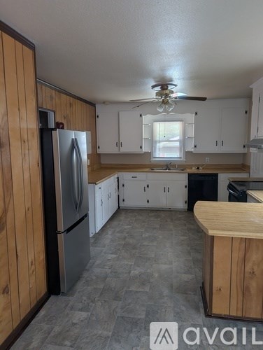 A kitchen with a refrigerator, cabinets, and a ceiling fan.