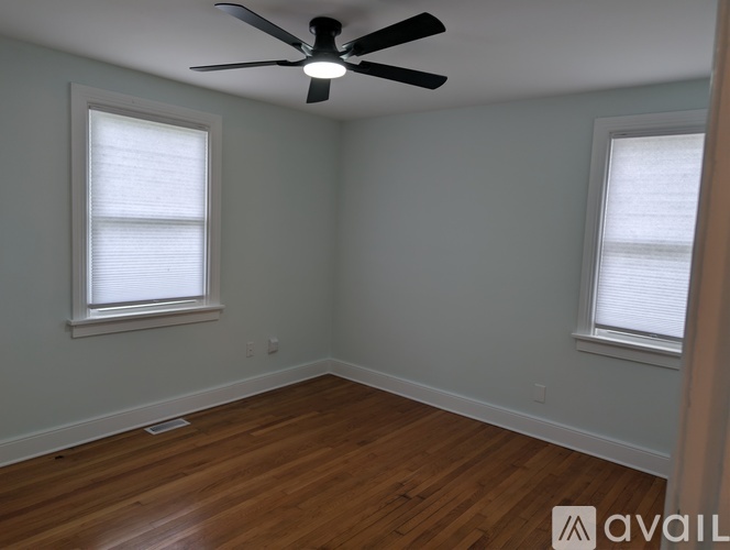 A room with a ceiling fan and two windows.