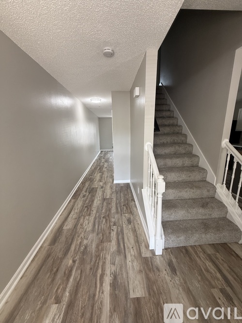 A hallway with a staircase and wooden flooring.