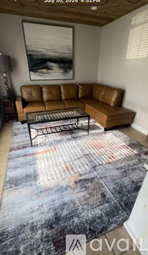 A living room with a brown leather couch and a large abstract painting on the wall.