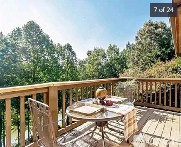 A wooden table with chairs is set on a deck with a view of trees.