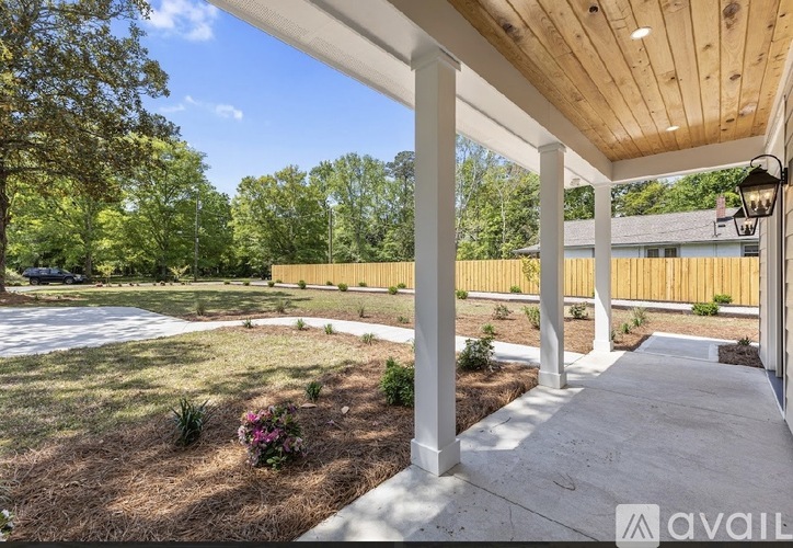 A porch with a white railing and pillars is surrounded by a grassy area and trees.