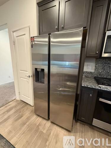 A stainless steel refrigerator stands in a kitchen with wooden flooring.