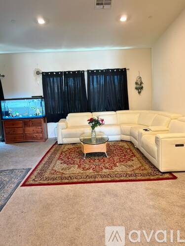 A living room with a white sofa set and a glass coffee table with a vase of flowers on it.