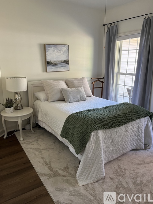 A bedroom with a large bed and a small table with a lamp.