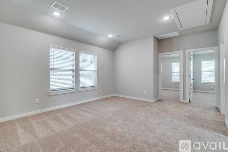 A spacious room with beige carpeting and two windows with blinds.