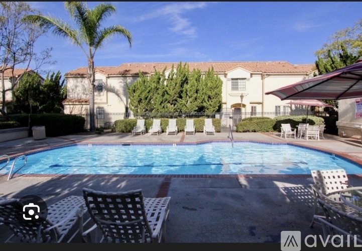 A pool surrounded by chairs and trees with a house in the background.