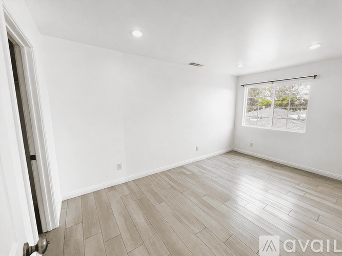 A spacious room with wooden flooring and a window with blinds.