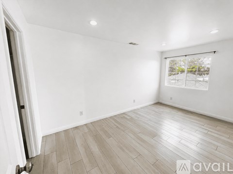 A spacious room with wooden flooring and a window with blinds.