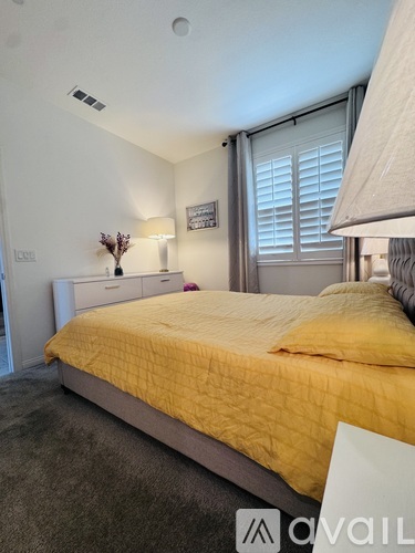 A bedroom with a bed covered in yellow bedding and a white nightstand with a lamp.