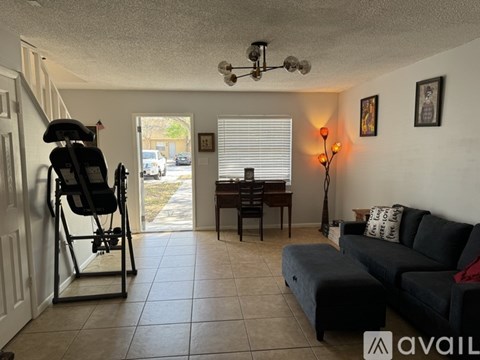 A living room with a black couch, a chair, a table, and a window with blinds.