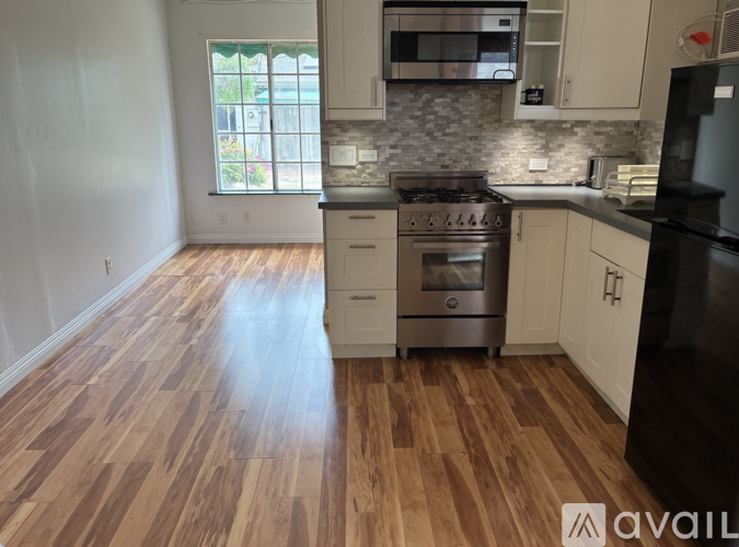A kitchen with wooden floors and a black refrigerator.