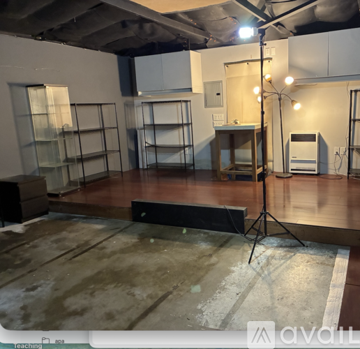 A room with a wooden floor and a white wall with a black speaker on a stand.
