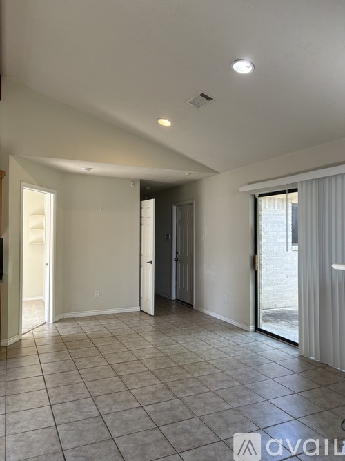 A spacious room with tiled flooring and a sliding glass door leading outside.