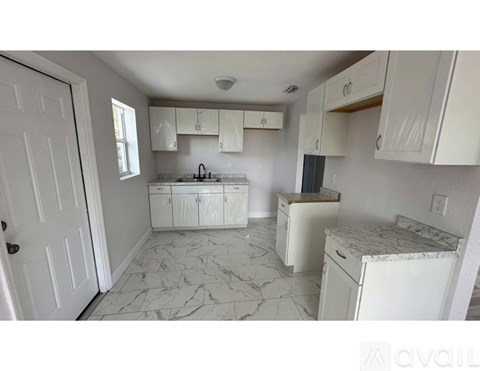 A kitchen with white cabinets and marble flooring.